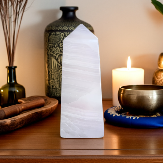 Mangano calcite obelisk from Peru displayed on dresser with singing bowls, candles in spiritual home decor arrangement